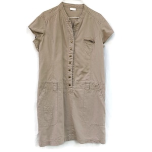 Può includere: Un abito beige a maniche corte con bottoni sul davanti e tasche. L'abito è appeso a un'appendiabiti bianca su uno sfondo bianco.