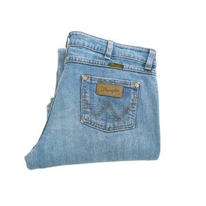 May include: A pair of light blue denim jeans folded in half, with a brown leather patch that says "Wrangler" on the back pocket.