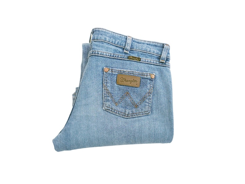 May include: A pair of light blue denim jeans folded in half, with a brown leather patch that says "Wrangler" on the back pocket.