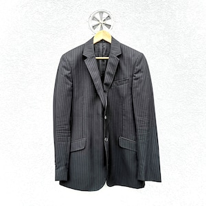 May include: A black pinstripe blazer hanging on a wooden hanger against a white wall.