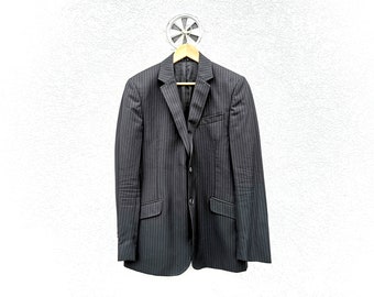 May include: A black pinstripe blazer hanging on a wooden hanger against a white wall.