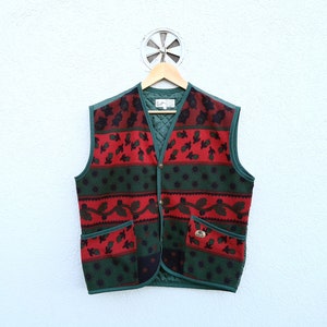 May include: A sleeveless vest with a quilted green lining and trim. The front features a pattern of red and black floral designs on a green background. It has two pockets and is fastened with three buttons.
