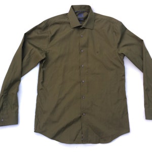 Puede incluir: Camisa de manga larga verde oliva. Presenta un cuello clásico, puños abotonados y un corte entallado. La camisa tiene botones en la parte delantera y está confeccionada con una tela de color liso, adecuada para uso informal o semiformal.