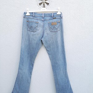 May include: A pair of light blue denim jeans with a bootcut leg. The jeans have a brown leather patch on the back with the Wrangler logo.