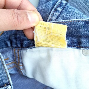 May include: A close-up of a blue denim jean pocket with a yellow care label that reads "15L 1038 40%".