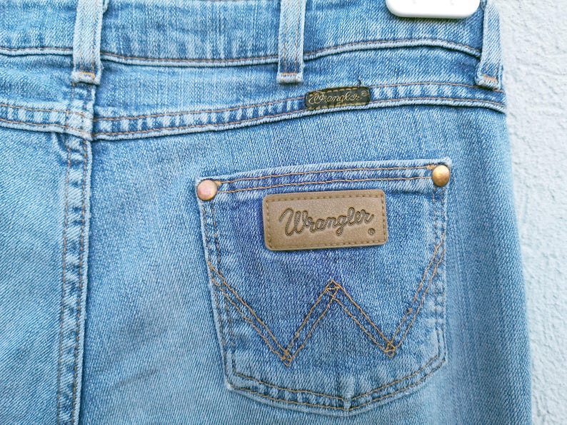 May include: A pair of blue denim jeans with a brown leather patch that says "Wrangler" on the back pocket.