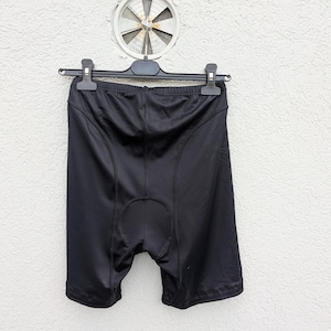 Puede incluir: Pantalones cortos de ciclismo negros confeccionados en tejido sint&eacute;tico liso con costuras visibles a lo largo de las caderas y una zona de la entrepierna reforzada y acolchada. Los pantalones cuelgan de una percha de pl&aacute;stico negra.