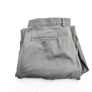 May include: A pair of grey folded trousers with a single back pocket and a button.