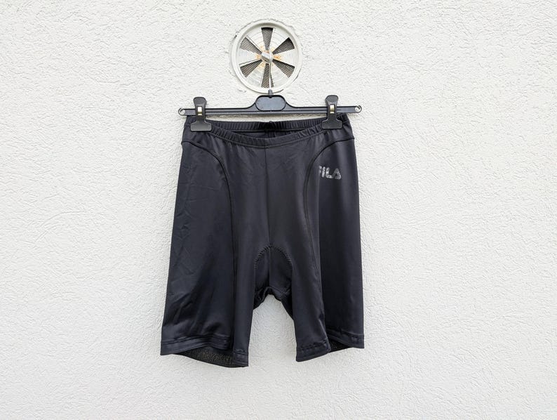 Puede incluir: Pantalones cortos deportivos negros con un corte ajustado y tejido el&aacute;stico liso. La prenda incluye una cintura el&aacute;stica negra y el logotipo de la marca FILA impreso en un tono gris oscuro en la parte superior del muslo izquierdo.