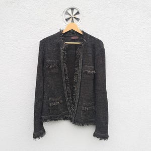 Può includere: Un cardigan di maglia nero con bordi sfrangiati e tasche. Il cardigan ha una lunghezza leggermente corta e una vestibilità rilassata.
