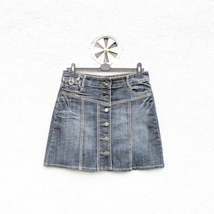 May include: A blue denim mini skirt with a button-down front and a classic five-pocket design. The skirt has a medium wash with subtle fading and light distressing. It hangs on a black hanger against a white wall.