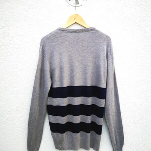 May include: A white ceramic mug with a black handle and the text "But First, Coffee" in a bold, black font. The mug is filled with a dark liquid, probably coffee, and rests on a light-coloured surface.