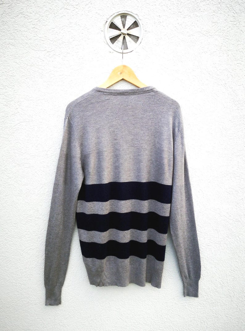 May include: A white ceramic mug with a black handle and the text "But First, Coffee" in a bold, black font. The mug is filled with a dark liquid, probably coffee, and rests on a light-coloured surface.