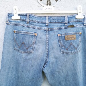May include: A pair of light blue denim jeans with a brown leather patch on the back pocket that says "Wrangler".