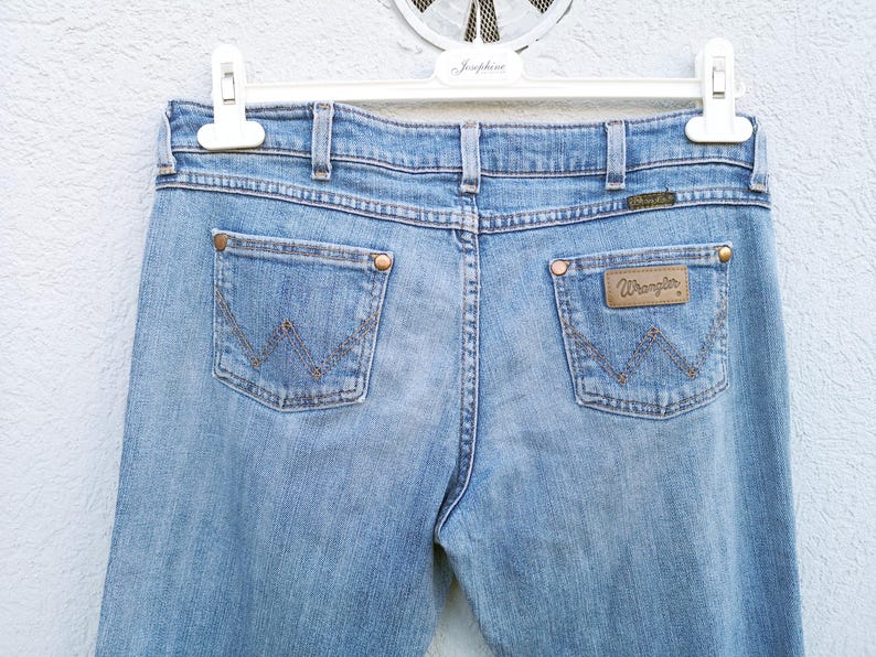 May include: A pair of light blue denim jeans with a brown leather patch on the back pocket that says "Wrangler".