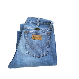 May include: A pair of blue denim jeans folded in half, showing the back pocket with a brown leather Wrangler label.