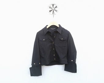 Puede incluir: Una chaqueta vaquera negra de manga larga y cierre de botones. La chaqueta tiene un corte corto y presenta una pequeña etiqueta en el lado izquierdo del pecho.