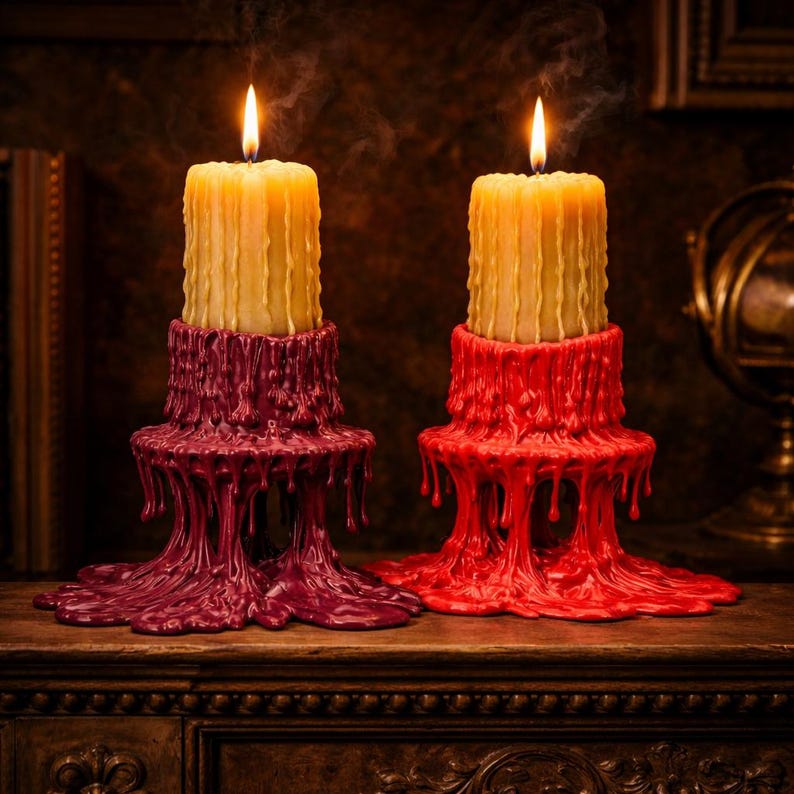 May include: Two lit pillar candles with a yellow hue, set atop decorative candle holders. One holder is a deep burgundy, the other is bright red. The holders have a melted wax design, creating a unique aesthetic.