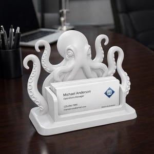 Può includere: Un portacarte da visita bianco a forma di polpo. Il supporto presenta un design dettagliato di polpo con tentacoli e una fessura per contenere biglietti da visita. I biglietti da visita riportano il nome "Michael Anderson" e le informazioni di contatto.