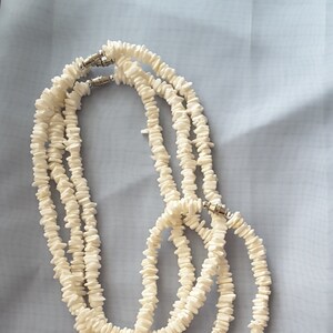 May include: A white shell necklace with multiple strands and silver clasps. The necklace is made of small, flat, white shell pieces.