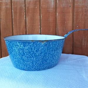 May include: A blue and white enamelware mixing bowl with a long handle. The bowl has a speckled pattern.