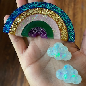May include: A rainbow-colored resin ornament with glitter, featuring a blue, green, purple, pink, gold, and orange color scheme. Two small, white, cloud-shaped resin ornaments with glitter are also included.