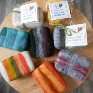May include: Six handmade soap bars wrapped in colorful felted wool. The soaps are arranged on a wooden surface. The labels on the soaps read "Wild Heart Handmade Soap".