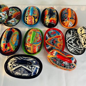 Puede incluir: Conjunto de jaboneras ovaladas de cerámica, pintadas con diseños coloridos y tapas a juego. Los colores vibrantes incluyen azul, rojo, naranja, verde y amarillo, creando un aspecto artístico y decorativo.