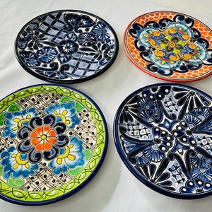 May include: Four colorful ceramic plates with intricate floral designs. The plates feature a variety of colors, including blue, green, orange, and white. The designs are traditional Mexican Talavera pottery.