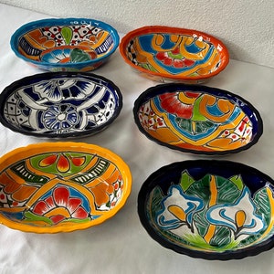 Op de afbeelding: Zes kleurrijke keramische kommen met ingewikkelde bloemmotieven. De kommen zijn ovaalvormig en hebben een geglazuurde afwerking. De ontwerpen bevatten een verscheidenheid aan kleuren, waaronder blauw, groen, rood, geel en wit.