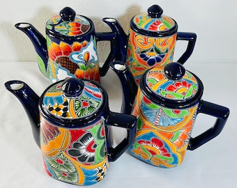 May include: Four ceramic teapots featuring vibrant, hand-painted floral and geometric patterns in shades of blue, orange, red, green, and yellow. Each teapot has a dark blue handle, spout, and lid with a matching knob, showcasing intricate designs.