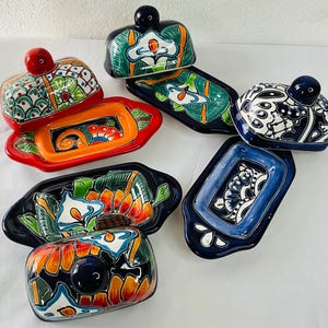 Puede incluir: Conjunto de cinco mantequilleras de cerámica Talavera de colores. Cada plato presenta un diseño floral único con colores vibrantes como azul, verde, naranja y rojo. Los platos son perfectos para servir mantequilla u otros bocadillos pequeños.