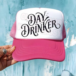 Peut inclure: Casquette de camionneur rose avec un panneau avant blanc et un lettrage noir pailleté qui dit "Day Drinker".