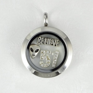 May include: A silver locket charm with a white background and a silver alien face, the number 51 with rhinestones, and the word "BELIEVE" in silver lettering.