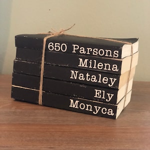 May include: A stack of five black books with white text on the spines. The books are tied together with twine. The text on the spines reads "650 Parsons", "Milena", "Nataley", "Ely", and "Monyca".