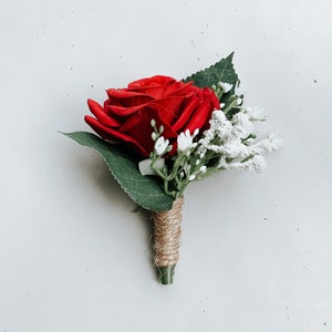 May include: A red rose buttonhole with white baby's breath and green leaves tied with twine.