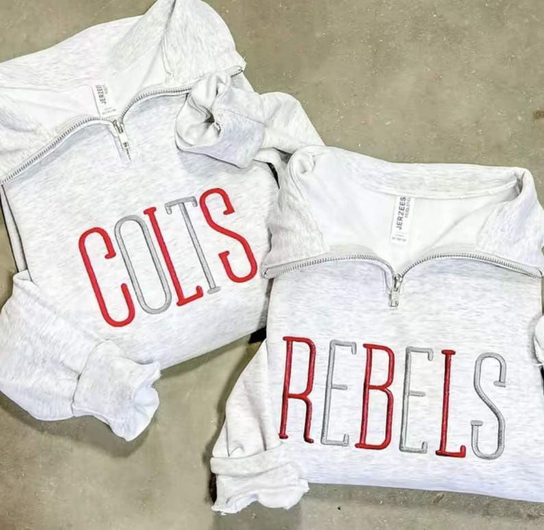 Peut inclure: Deux sweat-shirts gris clair avec des cols zipp&eacute;s. L'un porte le mot "COLTS" brod&eacute; en rouge et gris. L'autre porte le mot "REBELS" brod&eacute; en rouge et gris.