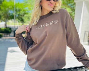 May include: A brown sweatshirt with the text "JESUS IS KING" in white lettering.