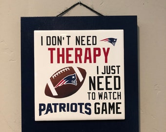Pode incluir: Uma placa branca com texto azul e vermelho e um gráfico de futebol. A placa diz "Eu não preciso de terapia, só preciso assistir aos Patriots jogarem".