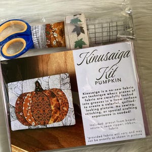 May include: A Kinusaiga Kit for a pumpkin craft project, packaged in clear plastic. The kit includes blue-handled scissors, various fabric strips with patterns, and a foam board with a printed image of a fabric-tucked pumpkin design.