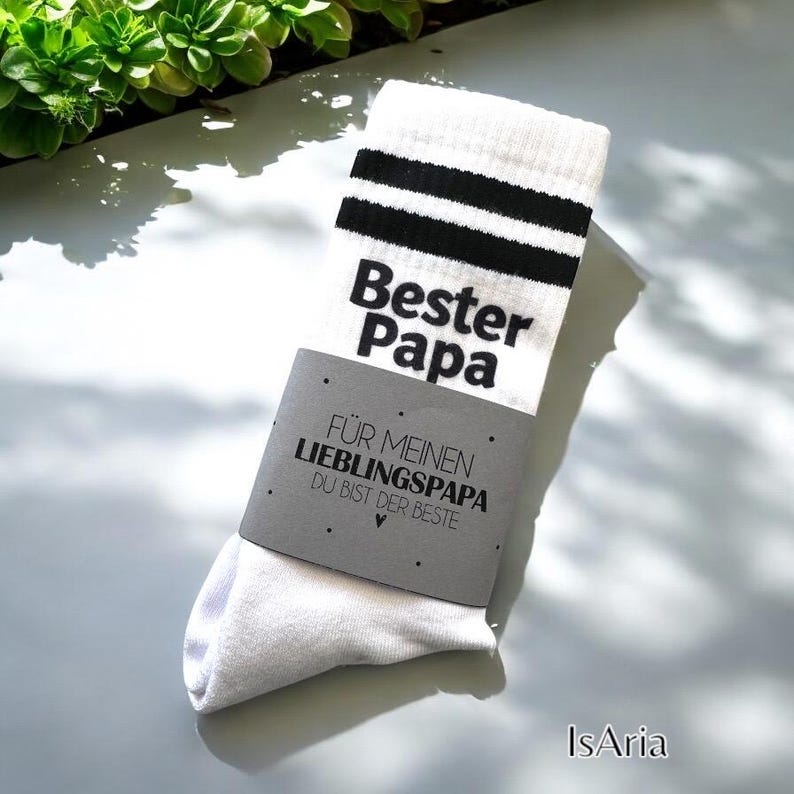Weiße Socken mit schwarzen Streifen und dem schwarzen Aufdruck "Bester Papa". Ein graues Etikett um die Socken zeigt "FÜR MEINEN LIEBLINGSPAPA DU BIST DER BESTE". Die Socken sind ein tolles Geschenk zum Vatertag oder Geburtstag.