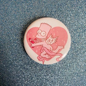 May include: A round button featuring a cartoon character as Cupid, with wings and a pink bow and arrow, set against a pink heart background. The button has a white border and is on a glittery blue surface.