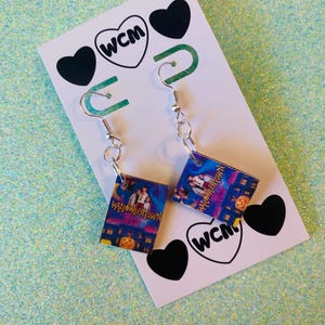May include: A pair of Halloween Town movie-themed earrings. Each earring features a rectangular charm with a movie poster design, silver-colored fish hook ear wires, and a white card with black heart and logo accents.