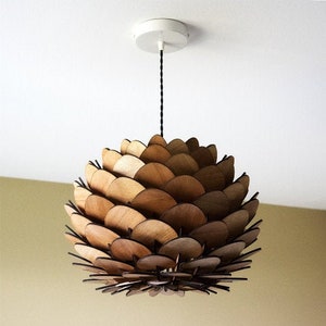 Puede incluir: Una lámpara colgante de madera con forma de piña con múltiples capas de madera.