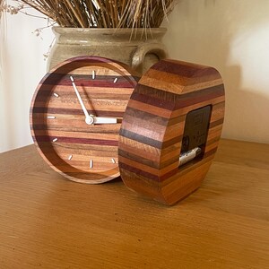 May include: Two wooden clocks with a striped design in shades of brown, red, and purple. The clock on the left has a white face with black hands. The clock on the right has a clear face with a black background.