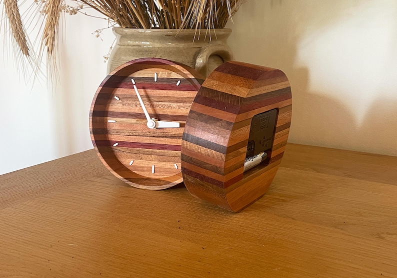 May include: Two wooden clocks with a striped design in shades of brown, red, and purple. The clock on the left has a white face with black hands. The clock on the right has a clear face with a black background.