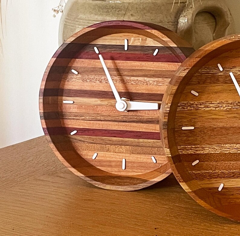 May include: Two round wooden clocks with white hands and white numbers. The clocks are made of different types of wood, creating a striped pattern.