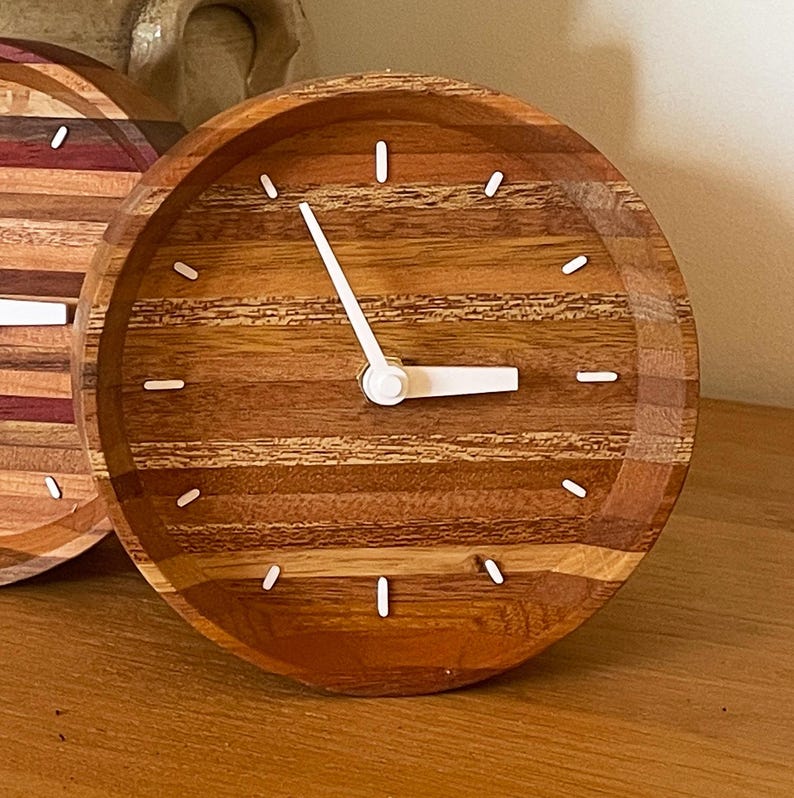 May include: A round wooden clock with white hands and white markings on a wood grain background.