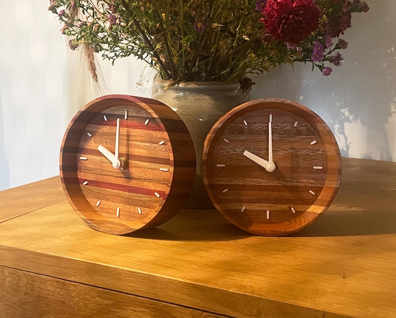 May include: Two wooden clocks with white hands and a striped wood design. The clocks are on a wooden surface.