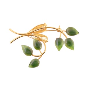 May include: A gold-toned brooch with a delicate wire design resembling a branch with five green gemstone leaves.